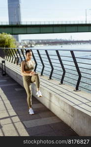 Pretty young woman in sportswear stretching on a river promenade