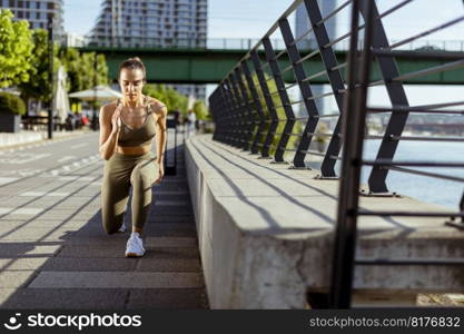 Pretty young woman in sportswear stretching on a river promenade