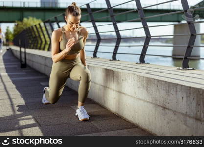 Pretty young woman in sportswear stretching on a river promenade