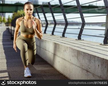 Pretty young woman in sportswear stretching on a river promenade