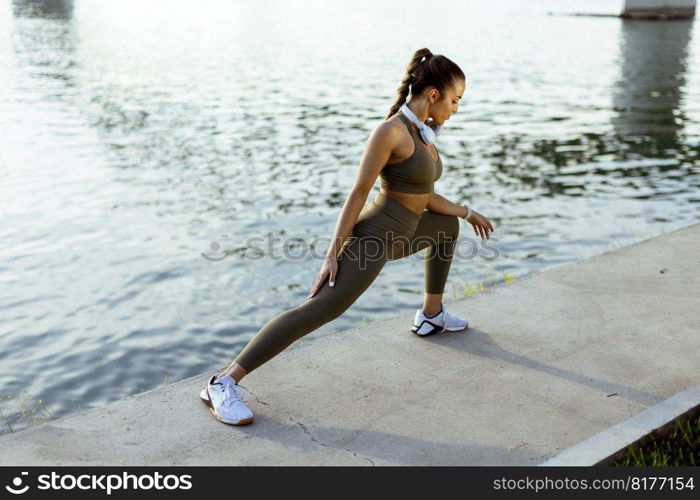 Pretty young woman in sportswear stretching on a river promenade