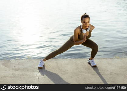 Pretty young woman in sportswear stretching on a river promenade