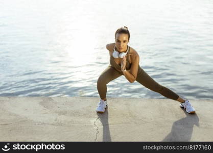 Pretty young woman in sportswear stretching on a river promenade