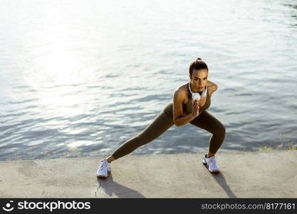 Pretty young woman in sportswear stretching on a river promenade