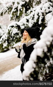 Pretty young woman in warm clothes enjoying in snow with takeaway coffee cup