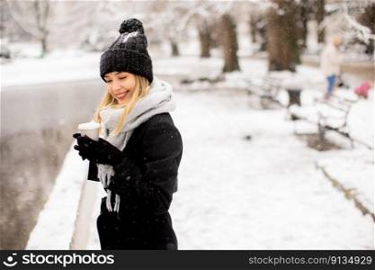 Pretty young woman in warm clothes enjoying in snow with takeaway coffee cup