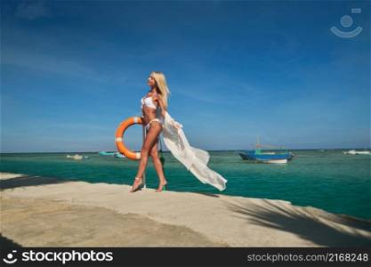 Pretty young woman in white pareo standing on pier near sea.. Pretty young woman in white pareo standing on pier near sea