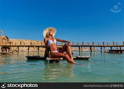 Pretty young woman in white swinsuit sitting on the bench sea pier.. Pretty young woman in white swinsuit sitting on the bench sea pier