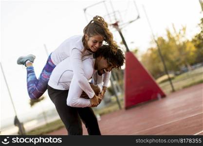 Pretty young woman jumping on the men shoulders at outdoor basketball court on a sunny day