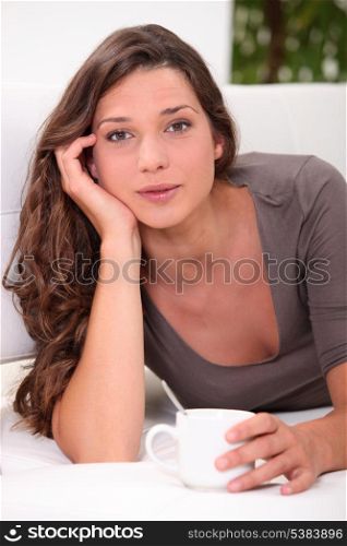 Pretty young woman laid with cup of coffee
