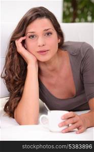 Pretty young woman laid with cup of coffee