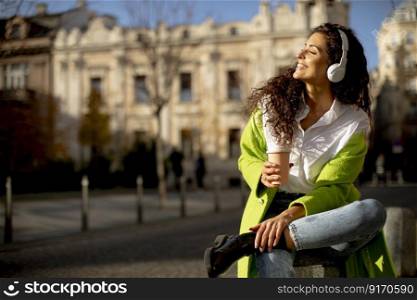 Pretty young woman listening music with smartphone on the street and holding takeaway coffee