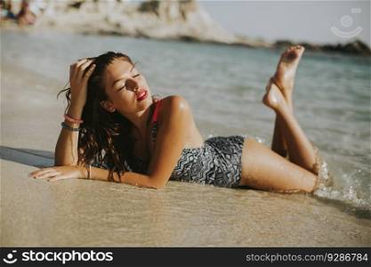 Pretty young woman lying in the water on the beach