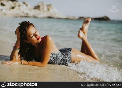 Pretty young woman lying in the water on the beach at sunny day
