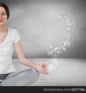 Pretty young woman meditating in empty room and graphic smoke, glitter and swirls are flying from her hand. Real deep meditation concept