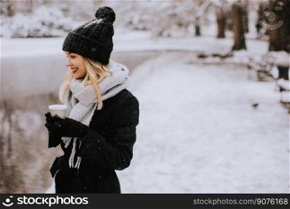 Pretty young woman n warm clothes enjoying in snow with takeaway coffee cup