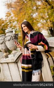 Pretty young woman on the street with coffee cup and mobile phone at autumn day