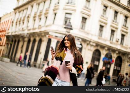 Pretty young woman on the street with coffee cup and mobile phone at autumn day