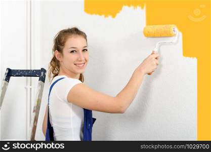pretty young woman paints the wall yellow color