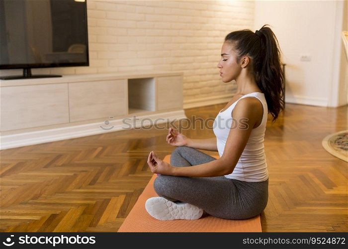 Pretty young woman practicing yoga lotus position in apartment