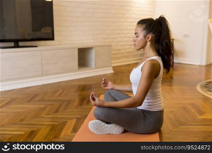 Pretty young woman practicing yoga lotus position in apartment