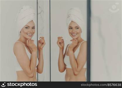 Pretty young woman reflected in mirror doing morning routine holds toothbrush while brushing teeth in bathroom at home, effective treatment for healthy white tooth. Personal oral care concept. Pretty woman reflected in mirror while brushing her teeth