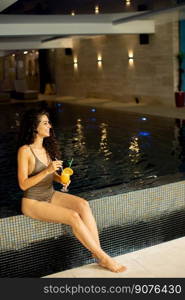 Pretty young woman relaxing and drinking orange juice on the poolside