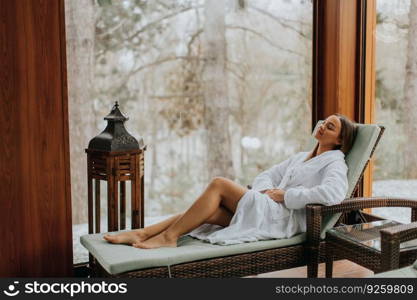 Pretty young woman relaxing in the deckchair by the indoor swimming pool at winter