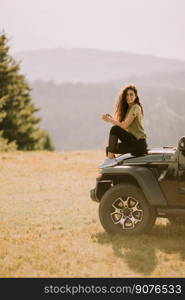 Pretty young woman relaxing on a terrain vehicle hood at countryside