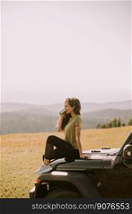 Pretty young woman relaxing on a terrain vehicle hood at countryside