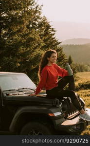 Pretty young woman relaxing on a terrain vehicle hood at countryside