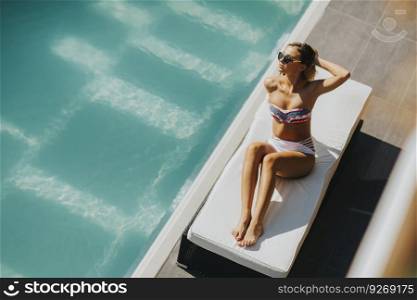 Pretty young woman relaxing on the bed by the swimming pool