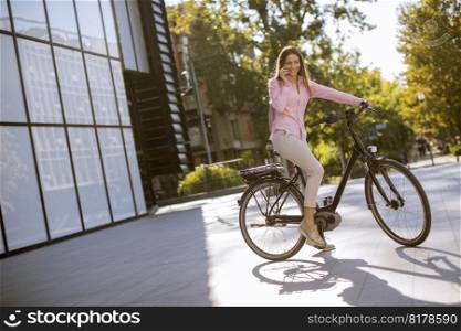 Pretty young woman riding an electric bicycle and using mobile phone in urban environment