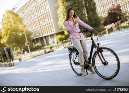 Pretty young woman riding an electric bicycle and using mobile phone in urban environment