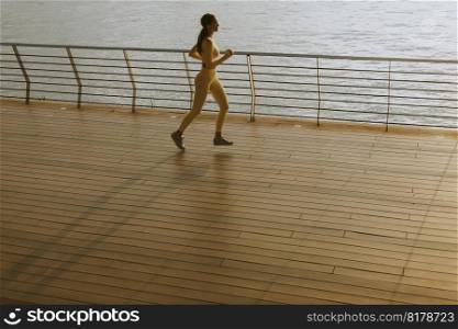 Pretty young woman running exercise on the riverside pier