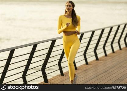 Pretty young woman running exercise on the riverside pier