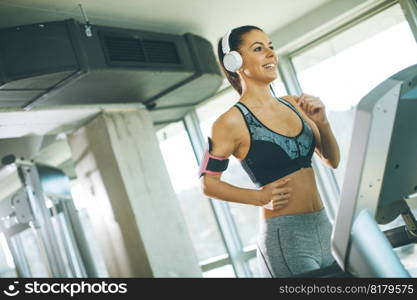 Pretty young woman running on treadmill during sports training in a gym