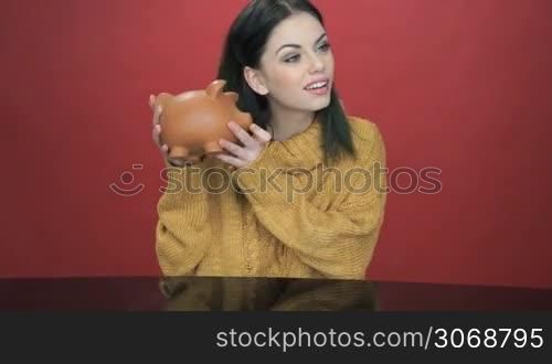 Pretty young woman shaking her piggy bank as she tries to decide if there is enough money inside to fulfil her dreams