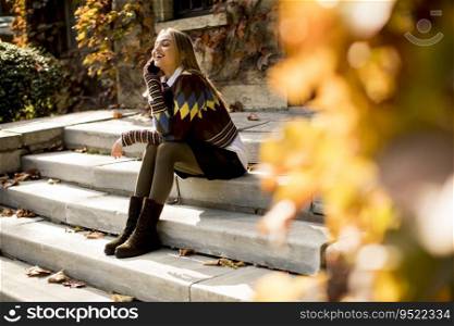 Pretty young woman sitting on a stairs with mobile phone in autumn park