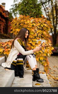 Pretty young woman sitting on a stairs with mobile phone in autumn park