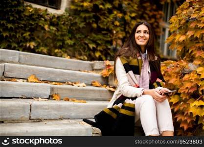 Pretty young woman sitting on a stairs with mobile phone in autumn park