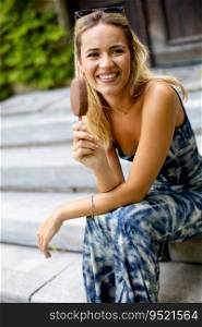 Pretty young woman sitting on stairs and eating ice cream on stick