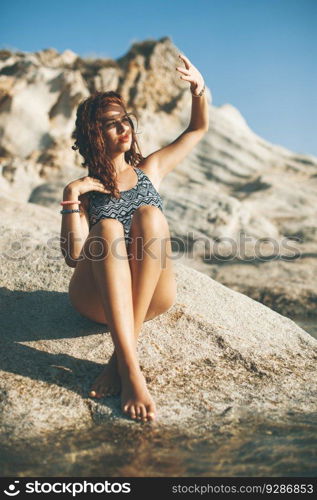 Pretty young woman sitting on the rocks at the beach