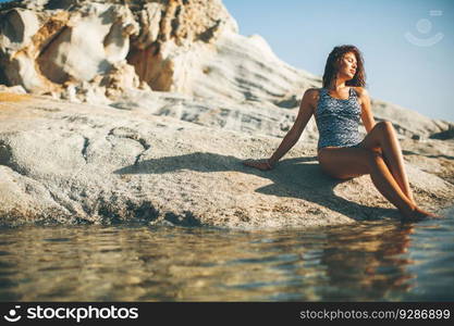 Pretty young woman sitting on the rocks at the beach