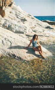 Pretty young woman sitting on the rocks at the beach