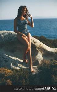 Pretty young woman sitting on the rocky shore by the sea on a sunny summer day