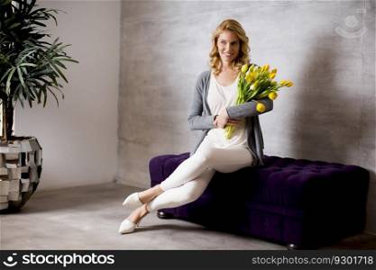 Pretty young woman sitting on the sofa with a bouquet of yellow tulips