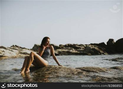 Pretty young woman sitting on the stony beach at the sea