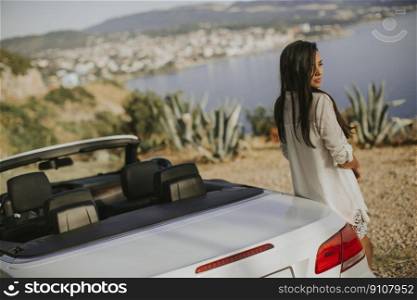 Pretty young woman standing by the white cabriolet car on a sunny day by the sea