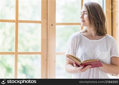 pretty young woman standing front window holding book